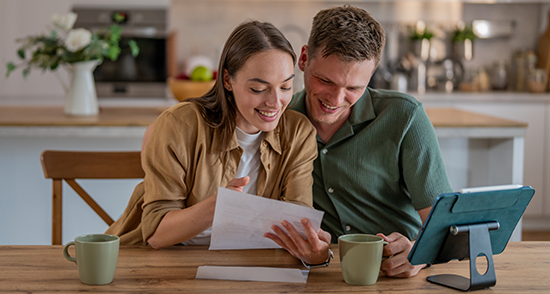 Couple sitting at their dining table with their ipad with cup of tea smiling at a letter